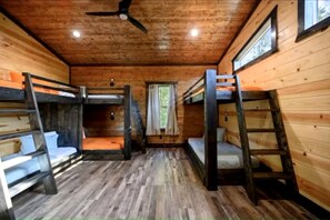 A cabin with bunk beds, wooden floors, a ceiling fan, and windows. - Surrounded by Tall Pines Forest Views with Hot Tub, Game Room & Outdoor Fireplace in Broken Bow, Oklahoma (Broken Bow)