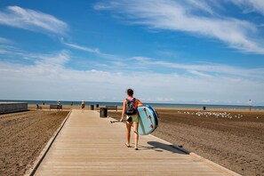 A wooden boardwalk leading to a beach with a person carrying a surfboard. - Impressive Waterfront Cottage with Fantastic Views in Leamington, Ontario (Leamington)