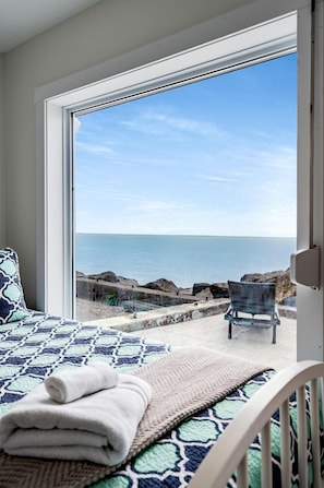 A bedroom with a large window, a bed with a patterned bedspread, a folded towel, and a chair outside. - Impressive Waterfront Cottage with Fantastic Views in Leamington, Ontario (Leamington)