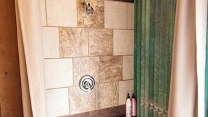 A shower area with a stone wall, wooden bench, and green curtains.
