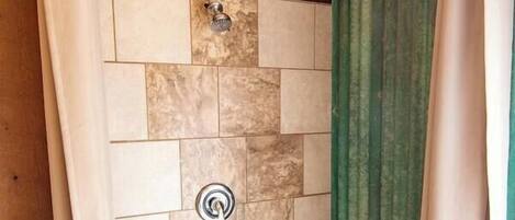 A shower area with a stone wall, wooden bench, and green curtains.