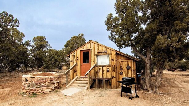 A rustic wooden cabin with a stone foundation, a wooden door, and a small porch.