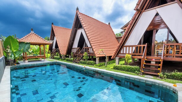 Piscina com deck revestido de azulejos, gazebos de madeira e um jardim exuberante.