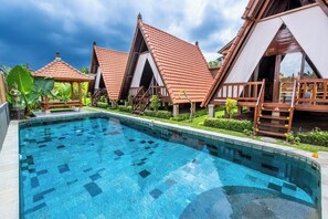 Ein Pool mit Fliesenveranda, Holzzelten und einem üppigen Garten.