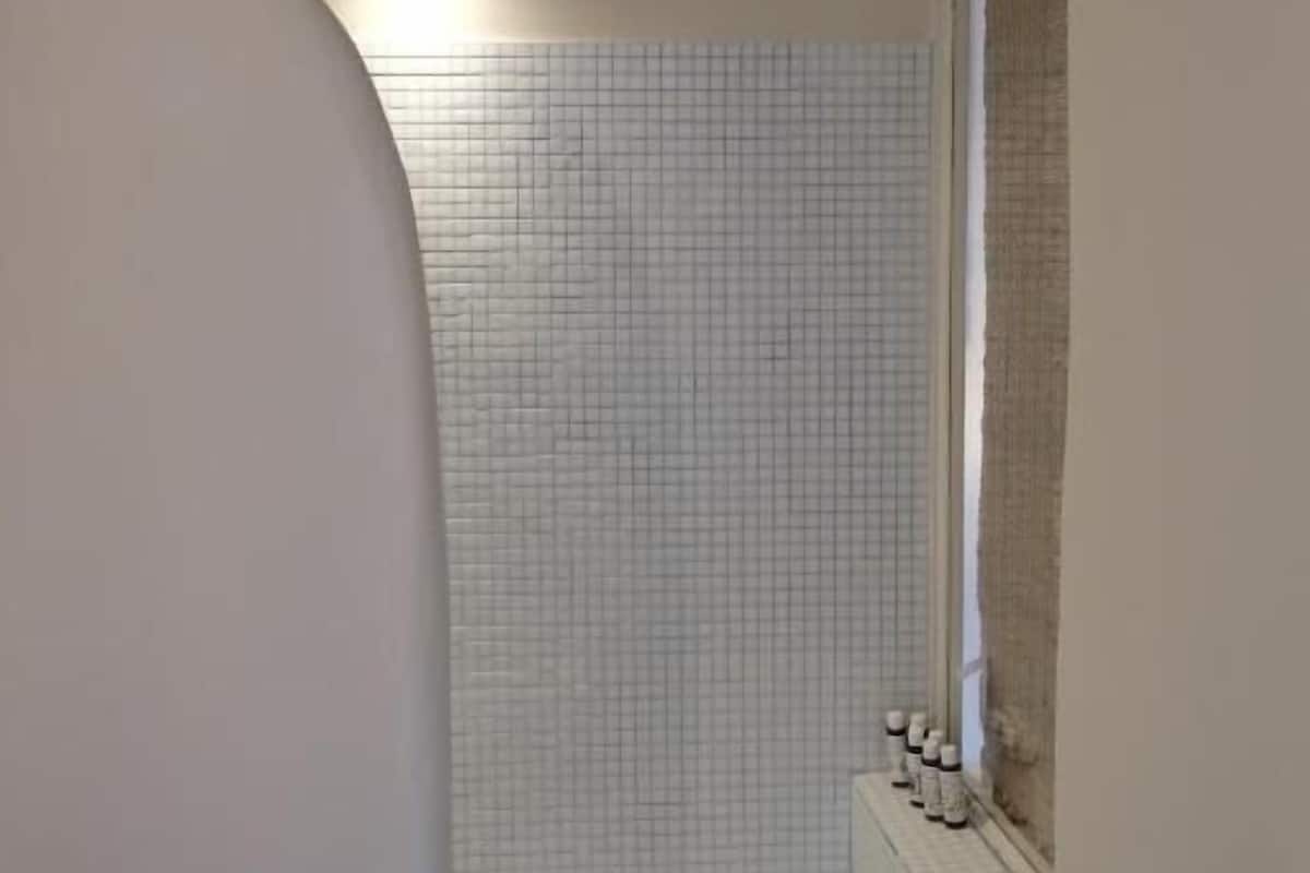 A bathroom with a tiled wall, a window, and a light fixture.