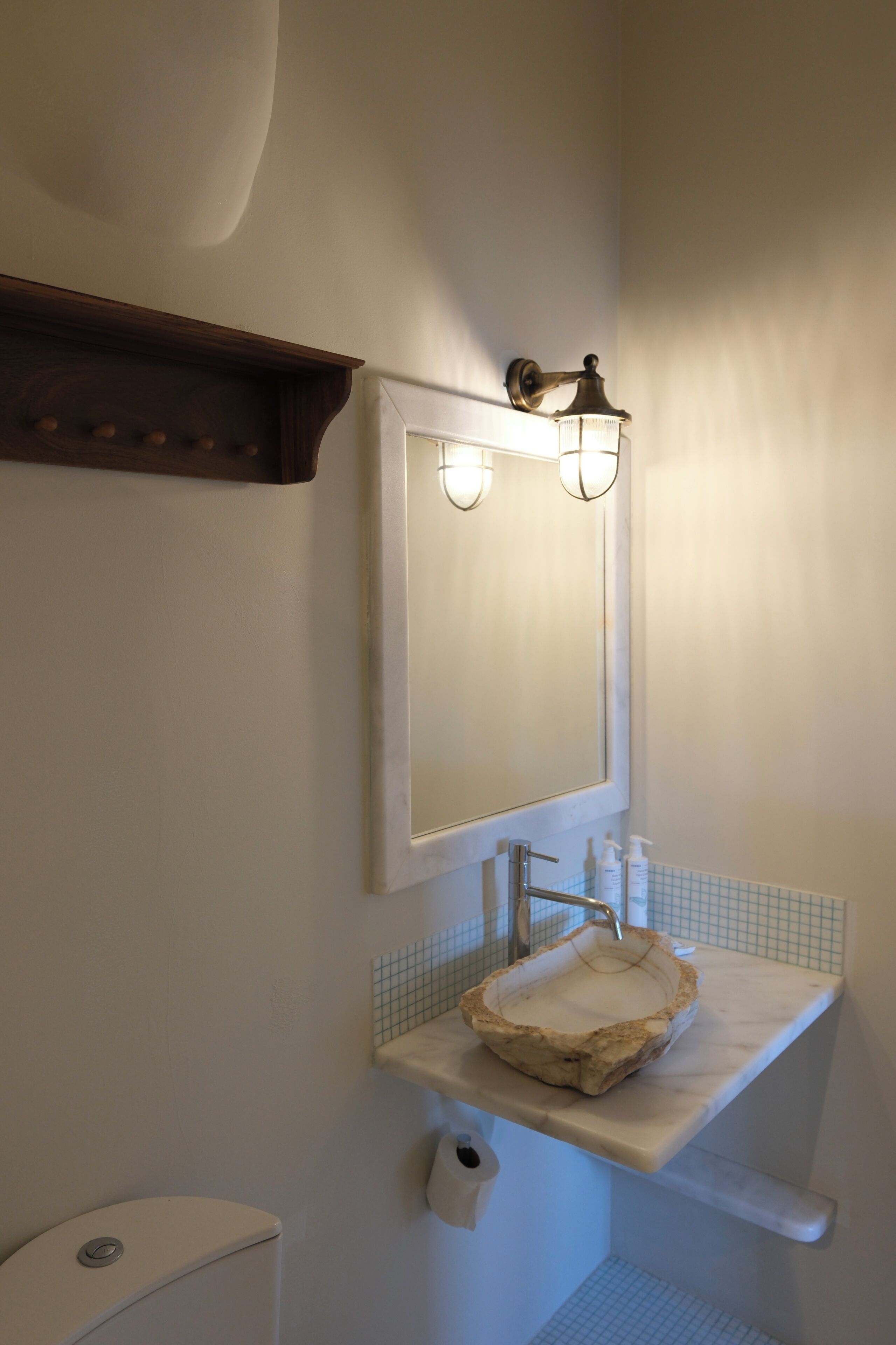 Een badkamer met een stenen wasbak, een spiegel en een wandlamp.