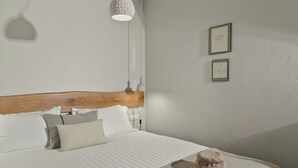 A neatly made bed with a wooden headboard, a single hat on the bed, and two framed pictures on the wall. - Mnimes Guesthouses Santorini  (Santorini)