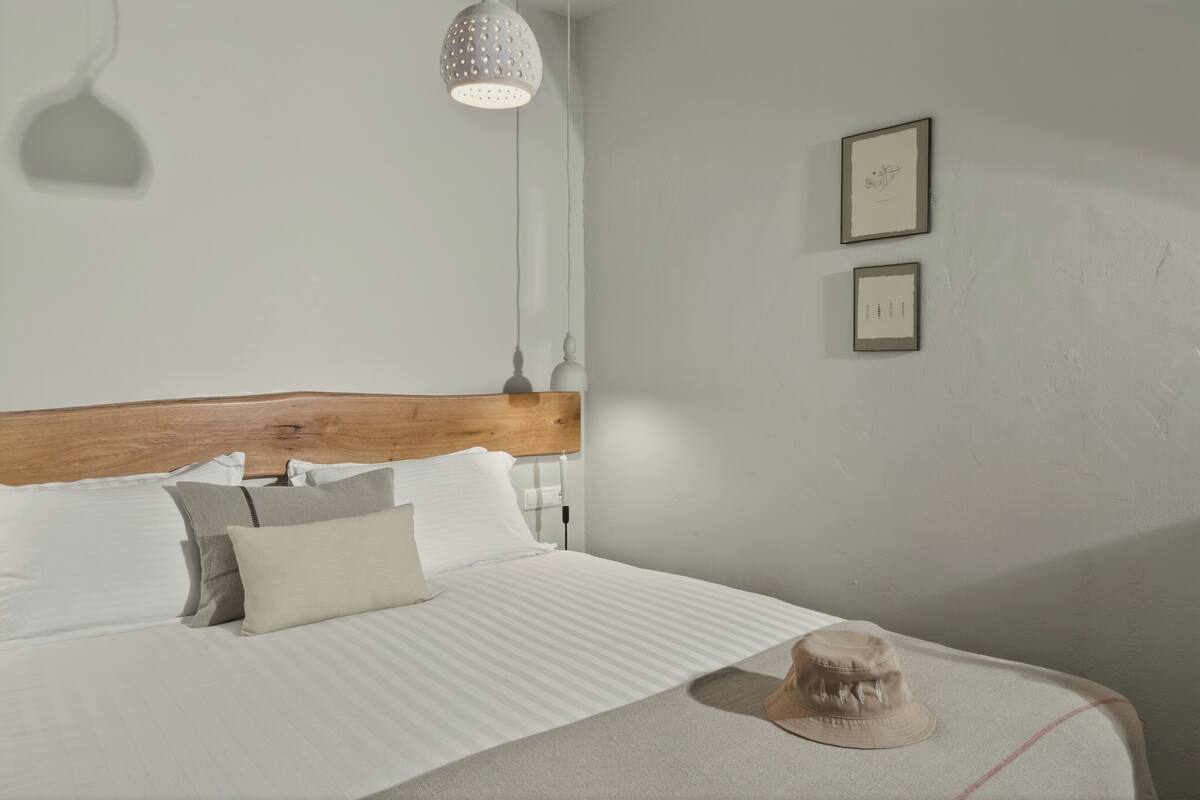 A neatly made bed with a wooden headboard, a single hat on the bed, and two framed pictures on the wall.