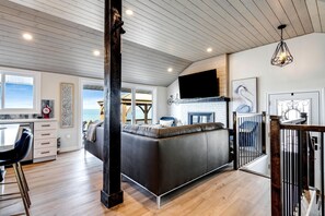 A modern kitchen with a large island, a dining area with bar stools, a fireplace, and a view of the sea.