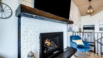 Une cheminée avec un décor en briques blanches, un fauteuil bleu et un plafond en bois.