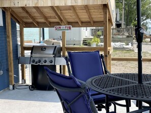 A covered outdoor area with a grill, two chairs, and a table.