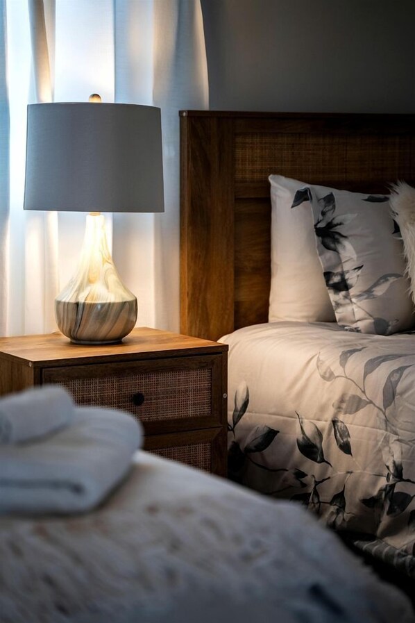 A bed with a floral-patterned duvet, a bedside lamp with a vase, and a wooden headboard.