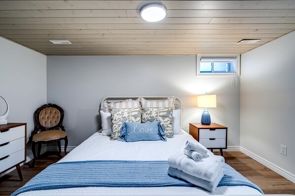 Un dormitorio con cama, silla, mesita de noche y ventana.
