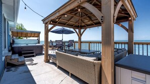 A covered outdoor seating area with a hot tub, wicker furniture, and a view of the ocean. - Modern Lake House with Incredible Deck and Jacuzzi in Ontario (Leamington)