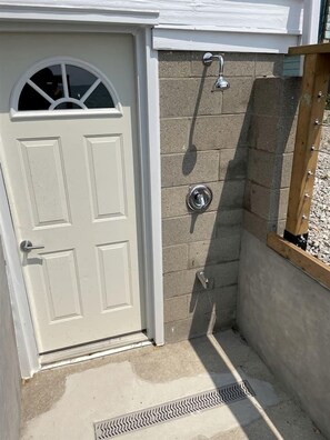 Una puerta blanca con un ventanal, una zona de ducha con estructura de madera y una pared de hormigón.
