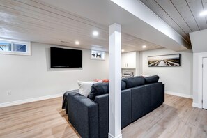 Een moderne woonkamer met een hoekbank, een flatscreen televisie en kunstwerken aan de muur.