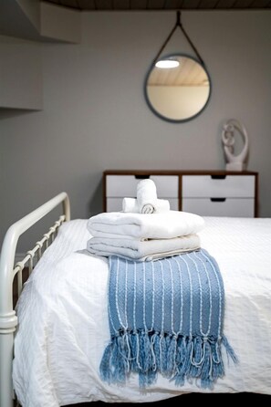 A neatly made bed with folded towels and a blue striped throw blanket.