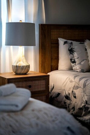 Una cama con edredón estampado de flores, una lámpara de noche con un florero y un cabecero de madera.