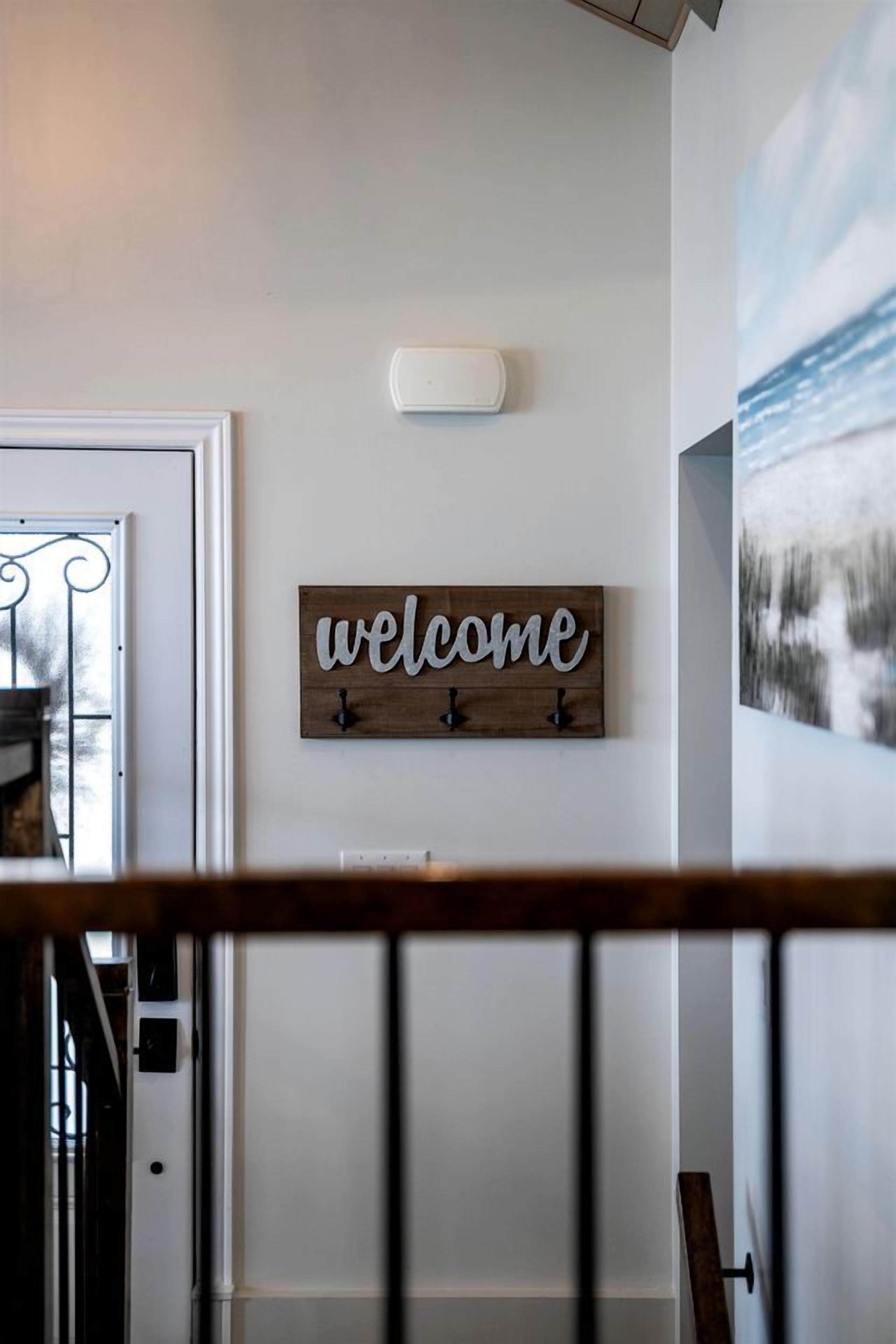 Un escalier avec une rampe en bois, une pancarte indiquant « Bienvenue » et un luminaire fixé au mur.