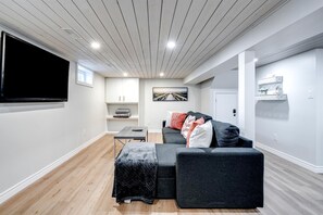 Una sala de estar moderna con un televisor de pantalla plana, un sofá, una mesita y un banco.