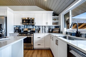 Una cocina moderna con armarios blancos, electrodomésticos de acero inoxidable y techo de madera.