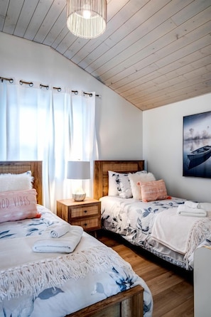 A bedroom with two beds, a wooden ceiling, a nightstand with a lamp, and a wall-mounted picture.