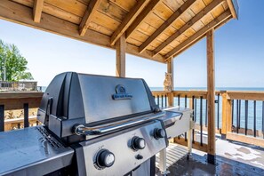 A Broil King grill on an outdoor deck with a wooden railing and a view of the sea.