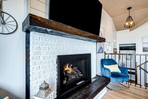 A fireplace with a white brick design, a blue chair, and a wooden ceiling. - Modern Lake House with Incredible Deck and Jacuzzi in Ontario (Leamington)
