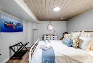 A bedroom with a bed, bedside table, lamp, and a painting of boats.