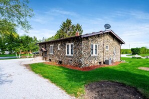 A stone house with a gravel driveway, surrounded by a well-maintained lawn and trees. - Stone Farm Retreat with Foosball and Poker Table in Ontario (Kingsville)