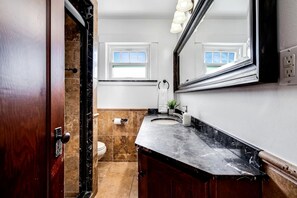 A bathroom with a marble sink, a toilet, a mirror, and a window. - Stone Farm Retreat with Foosball and Poker Table in Ontario (Kingsville)