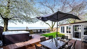 An outdoor deck with a hot tub, a table with chairs, and a patio umbrella. - Picturesque Oceanfront Cottage with Hot-tub in Leamington, Ontario (Leamington)