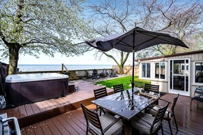 An outdoor deck with a hot tub, a table with chairs, and a patio umbrella. - Picturesque Oceanfront Cottage with Hot-tub in Leamington, Ontario (Leamington)
