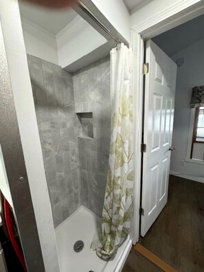 Eine Dusche mit Vorhang mit Blattmuster, eine weiße Tür und eine geflieste Wand.