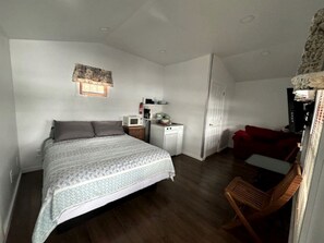 Ein Schlafzimmer mit einem Bett, einer kleinen Küchenzeile, einem roten Sofa und einem Holzstuhl.