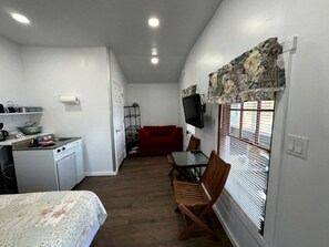 Ein kompakter Raum mit Küchenzeile, einer Essecke mit Tisch und Stühlen, einem roten Sofa und einem an der Wand befestigten Fernseher.