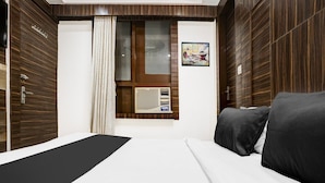A hotel room with a bed, a window with curtains, a wall-mounted air conditioning unit, and a framed picture. - Collection O Shirdi Near Sai Baba Temple (Rahata)