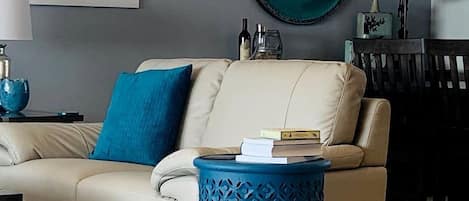 Een woonkamer met een bank, een ronde spiegel, een blauwe bijzettafel en een vloerkleed met dessin.