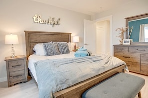 A bedroom with a bed, bedside tables, a bench, a dresser, and a wall sign.