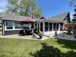 Ein Haus mit überdachter Terrasse, umzäunter Garten und kleinem Gartenbereich.
