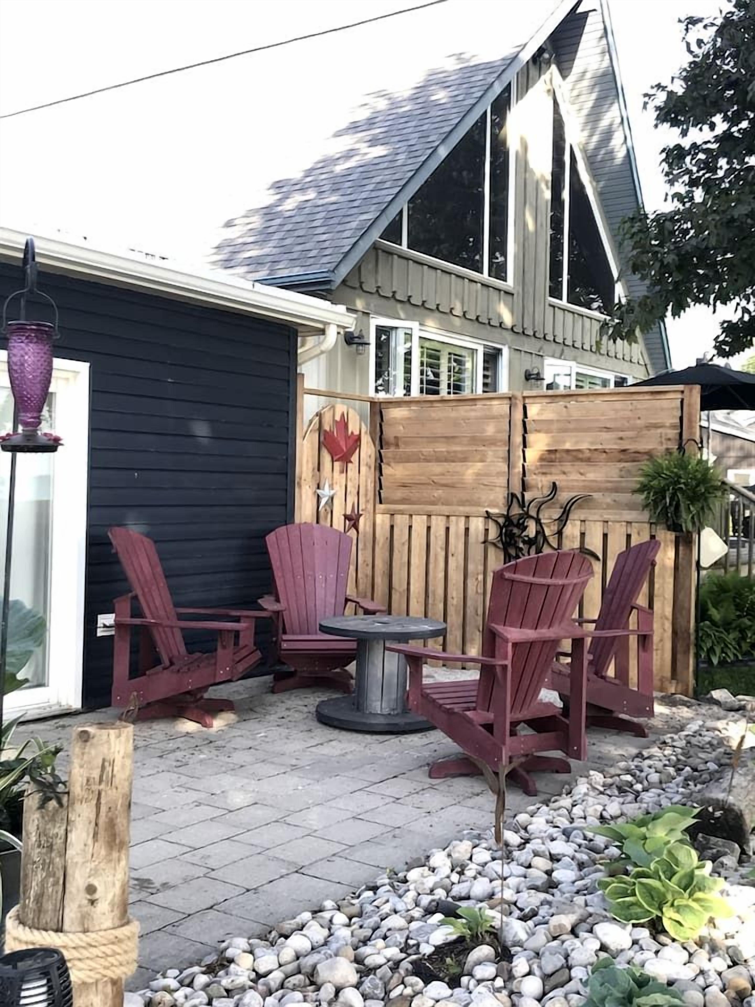 A patio with Adirondack chairs, a round table, and a wooden fence.