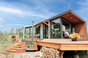 Une maison moderne avec de grandes fenêtres en verre, une terrasse en bois et un barbecue à l’extérieur.