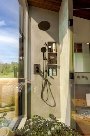 Une salle de bain moderne dotée d’une douche à parois de verre, d’une étagère intégrée pour les articles de toilette et offrant une vue sur l’extérieur.