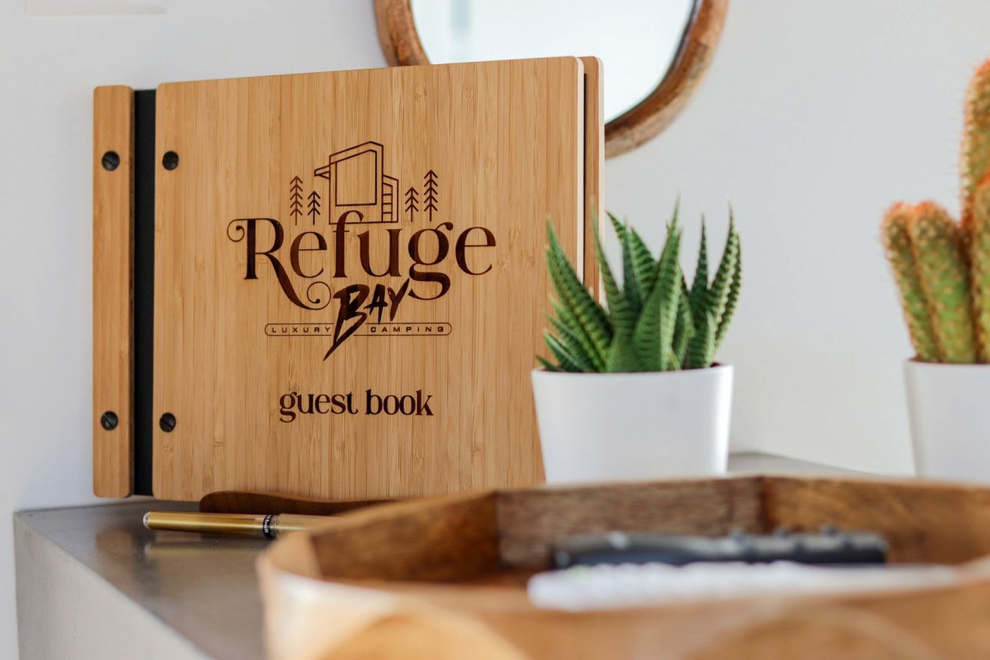 A wooden guest book with 'Refuge Bay Luxury Camping' engraved on it.