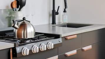 A modern kitchen with a stainless steel kettle on the stove, a faucet, and a bottle of hand soap.