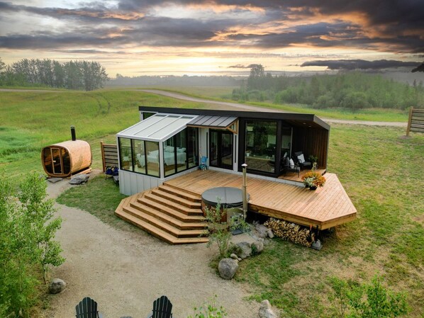 A modern cabin with a glass facade, wooden deck, and a hot tub.