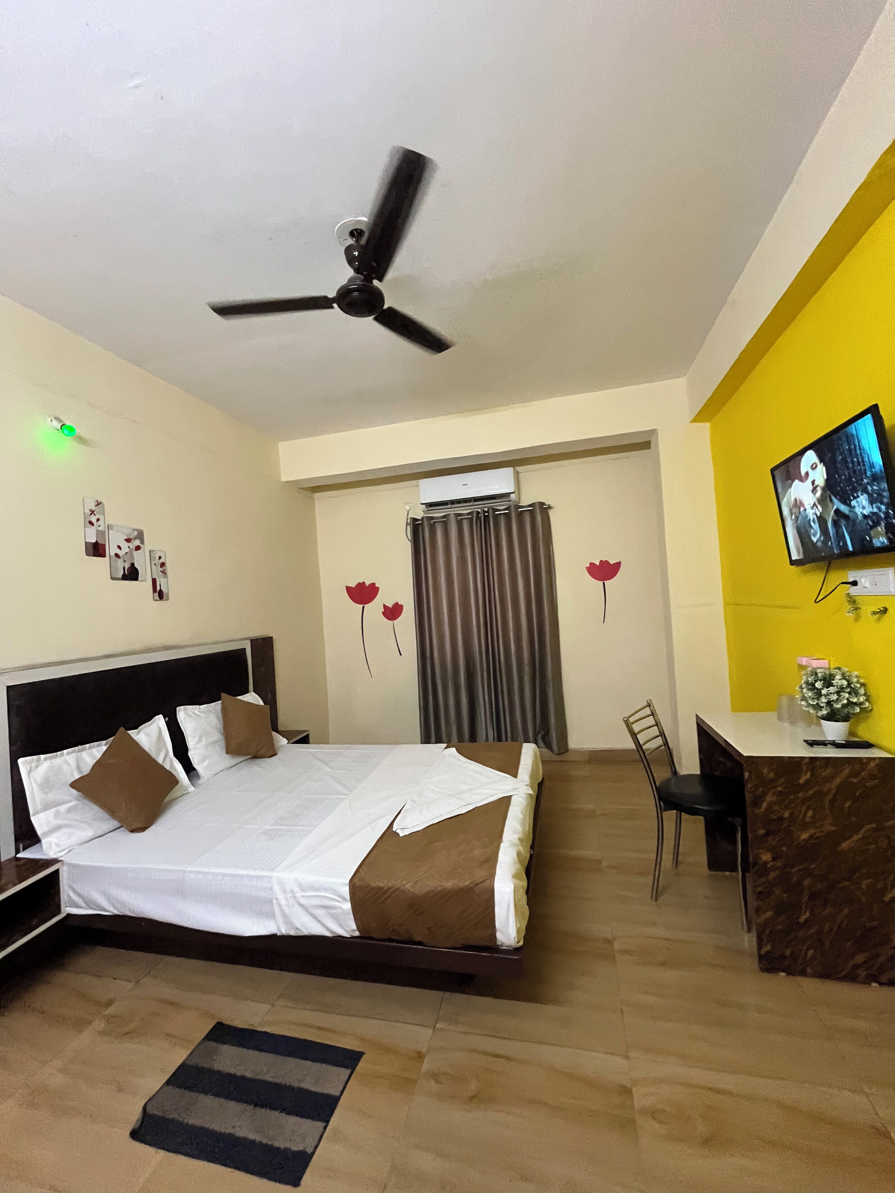 A hotel room with a bed, desk, chair, ceiling fan, air conditioning unit, and a television.