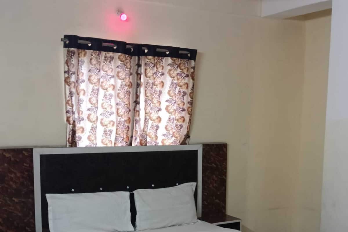 A single bed with a headboard, two bedside tables, and a window with patterned curtains.