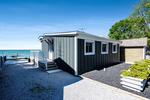 A small, single-story cabin with a covered porch and a set of steps leading to the entrance. - Gorgeous Cottage with Fire Pit and Nice Beach Vistas in Leamington, Ontario (Leamington)