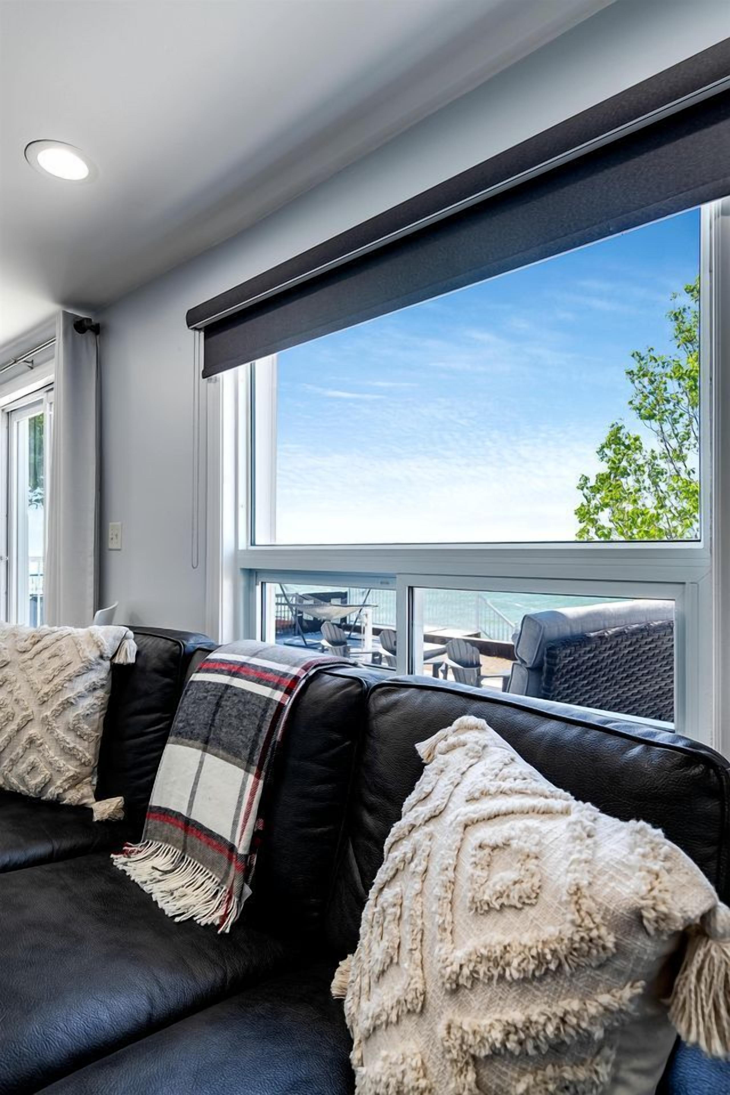 A modern living room with a black leather sofa, a large window with a view of the outdoors, and a ceiling light.